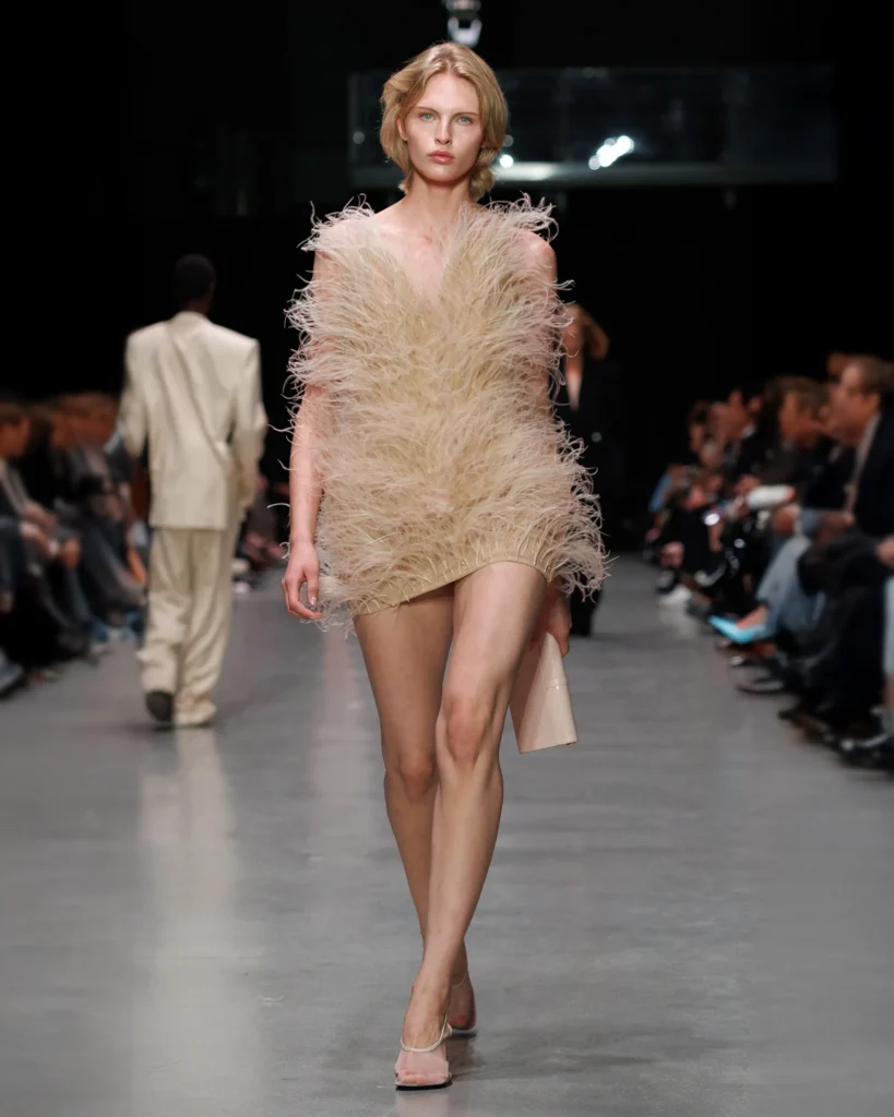 Model walking the runway at Paris Fashion Week in an ivory mini dress by Stella McCartney, featuring Fevvers’ plant-based feather alternative.